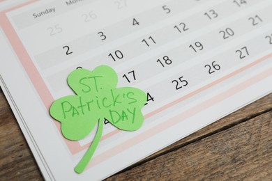 Photo of Paper clover leaf with words ST. PATRICK'S DAY and calendar on wooden background