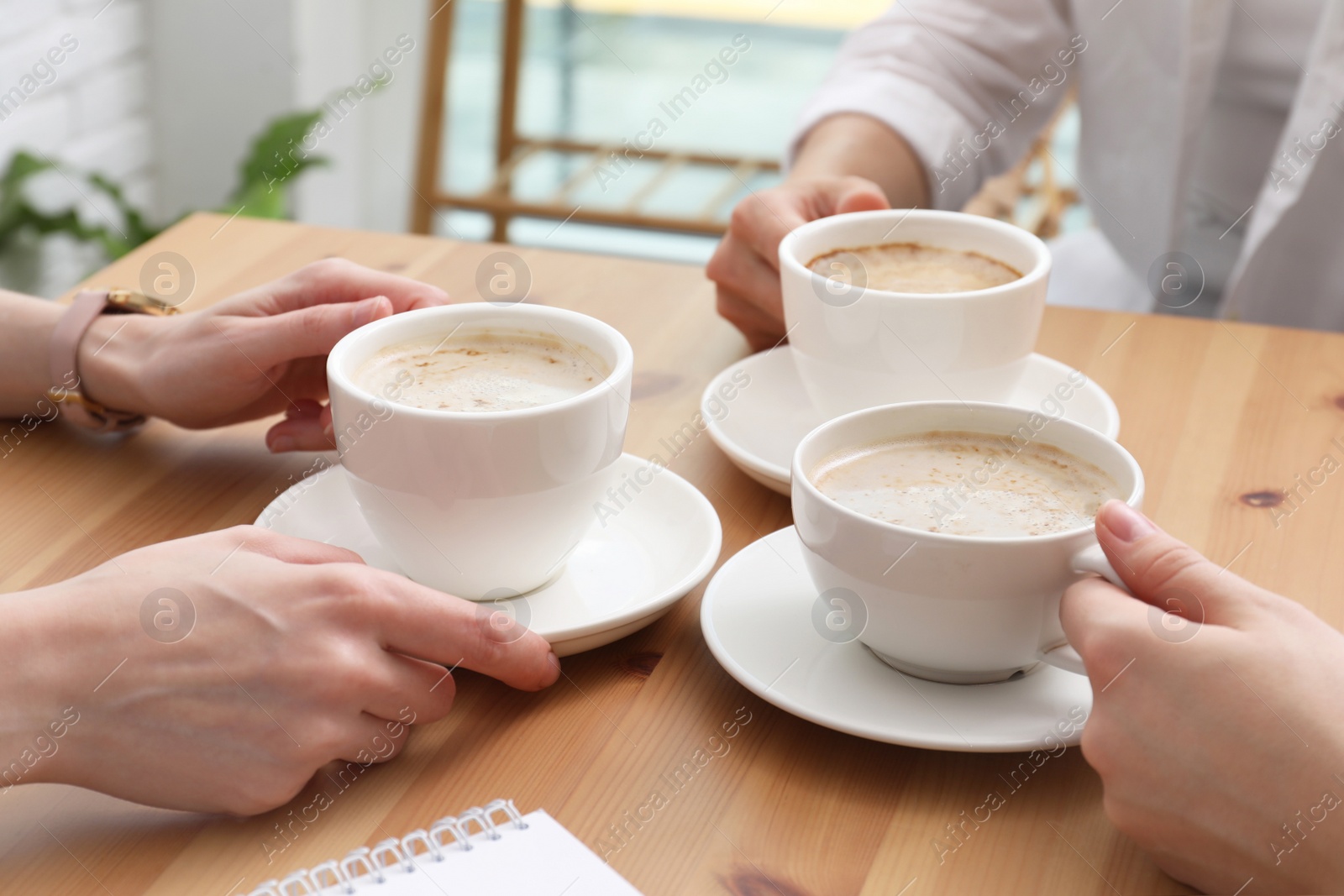 Photo of Women with cups of coffee at table in cafe, closeup