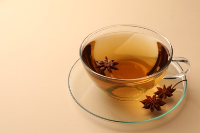 Photo of Glass cup of aromatic tea with anise stars on beige background. Space for text