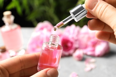 Photo of Woman dripping rose essential oil into bottle over table, closeup