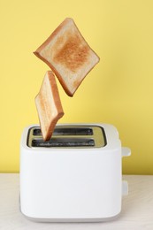 Photo of Bread slices popping up from modern toaster on white wooden table