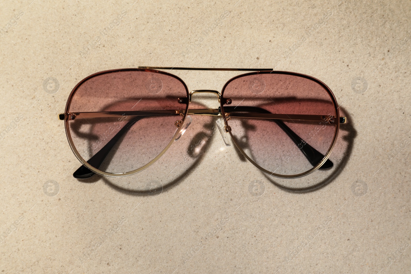 Photo of New stylish sunglasses on sand, top view