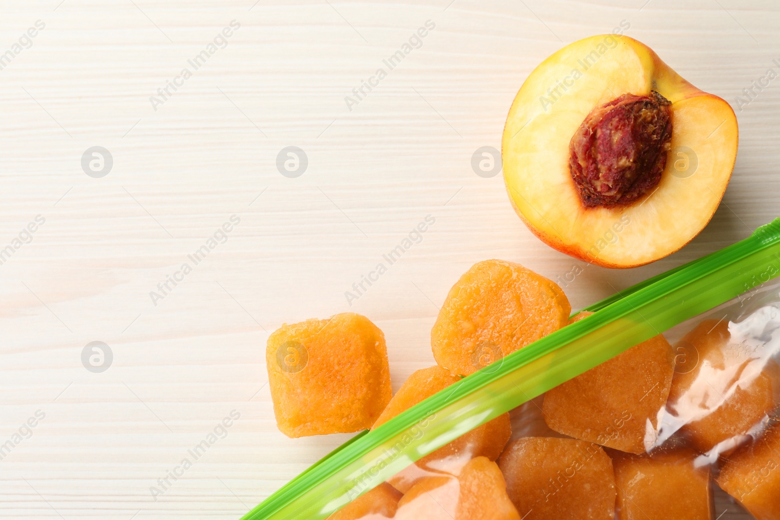 Photo of Frozen nectarine puree cubes in plastic bag and fruit on white wooden table, flat lay. Space for text