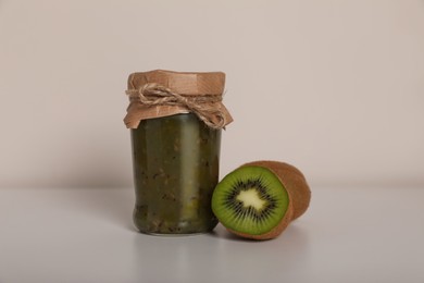 Photo of Tasty canned kiwi jam and fresh fruits on white background