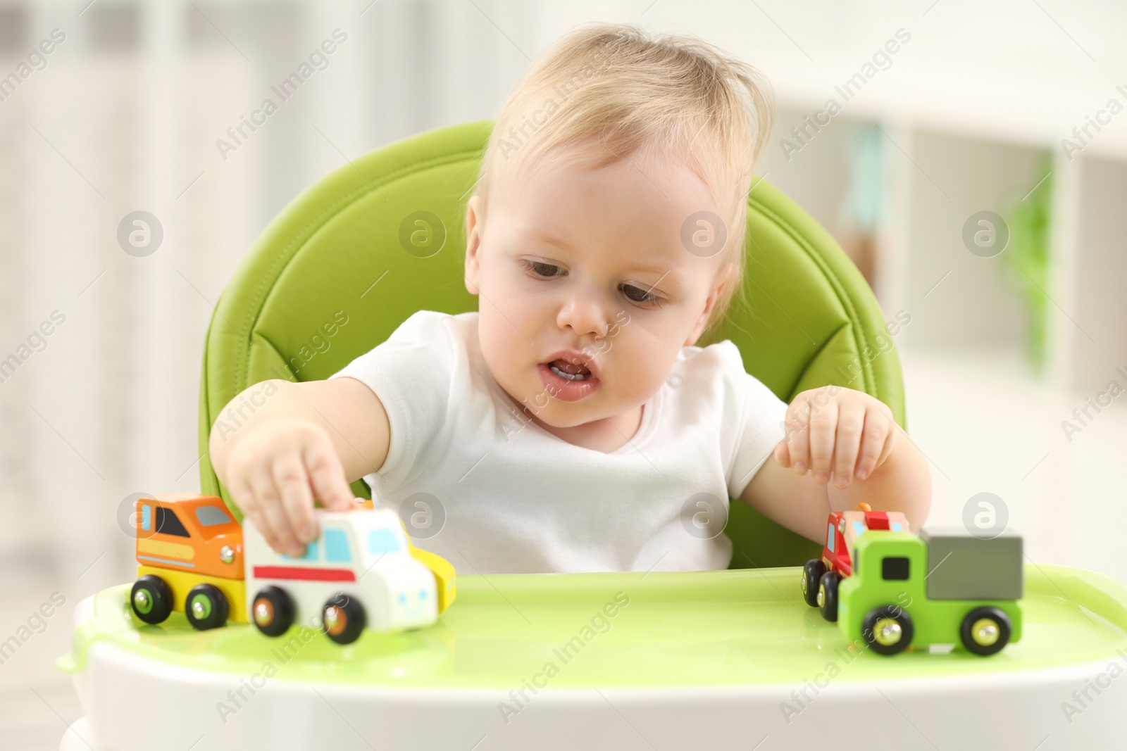 Photo of Children toys. Cute little boy playing with toy cars in high chair at home