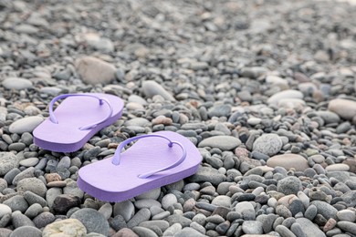 Photo of Stylish flip flops on pebble seashore. Space for text