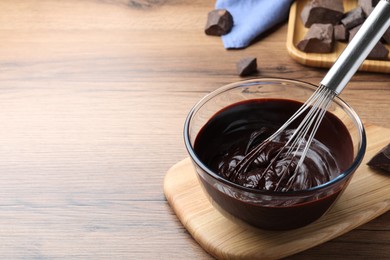 Delicious chocolate cream and whisk in glass bowl on wooden table, space for text