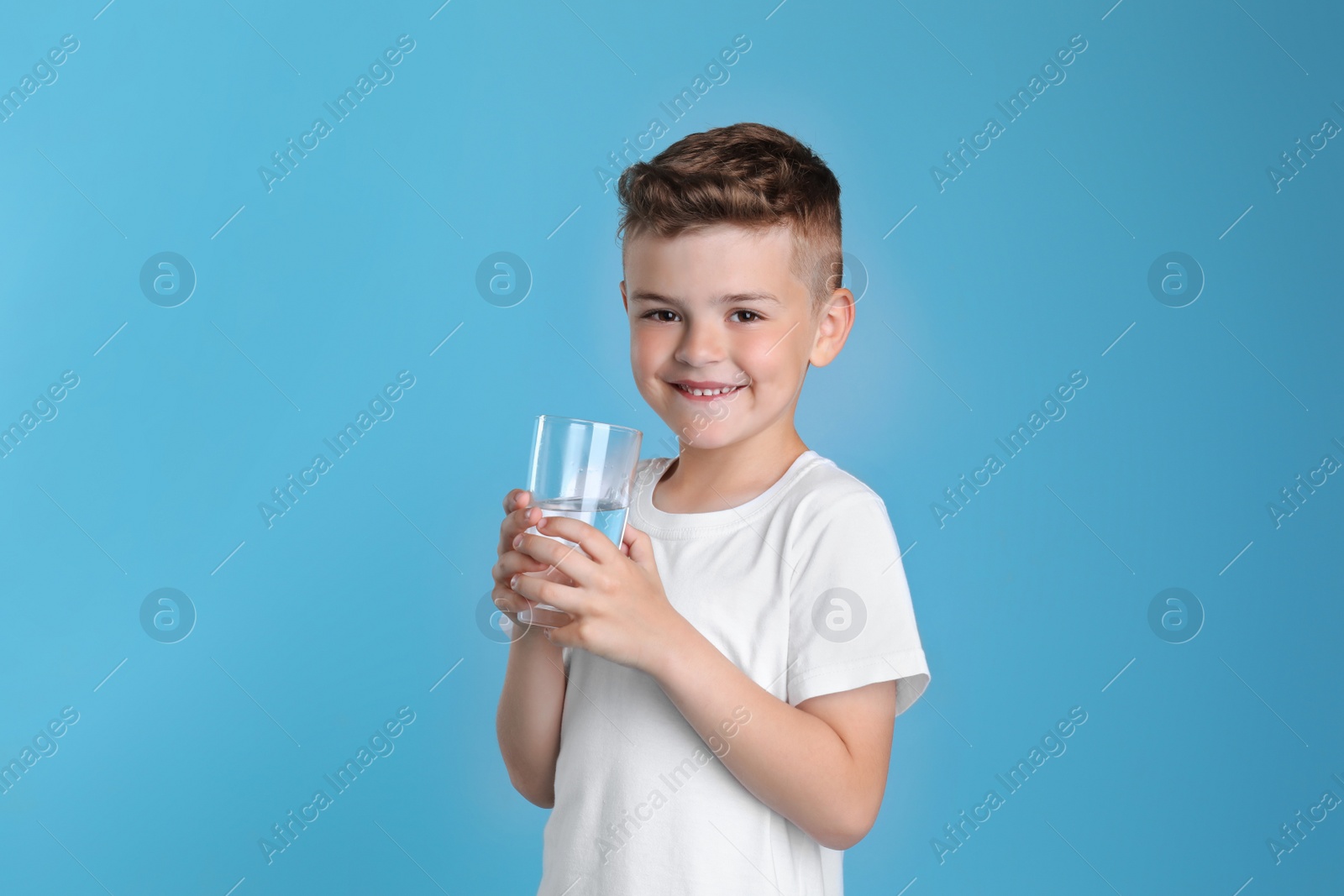 Photo of Cute little boy with glass of water on light blue background