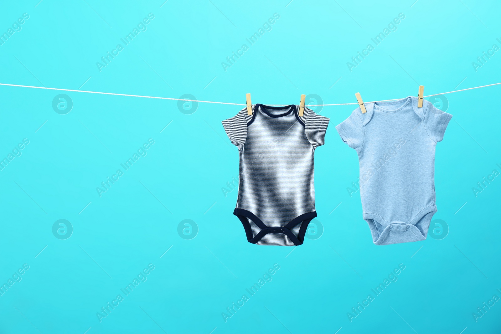 Photo of Colorful baby onesies hanging on clothes line against blue background, space for text. Laundry day