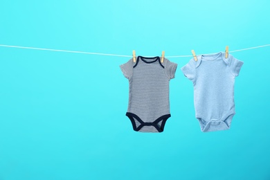 Colorful baby onesies hanging on clothes line against blue background, space for text. Laundry day