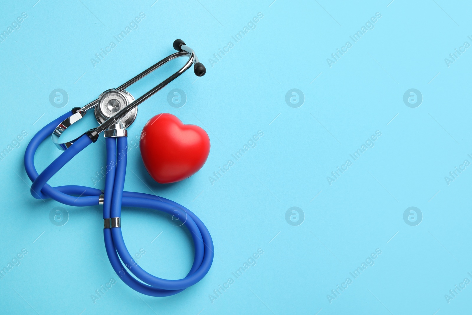 Photo of Stethoscope and red heart on light blue background, top view. Space for text