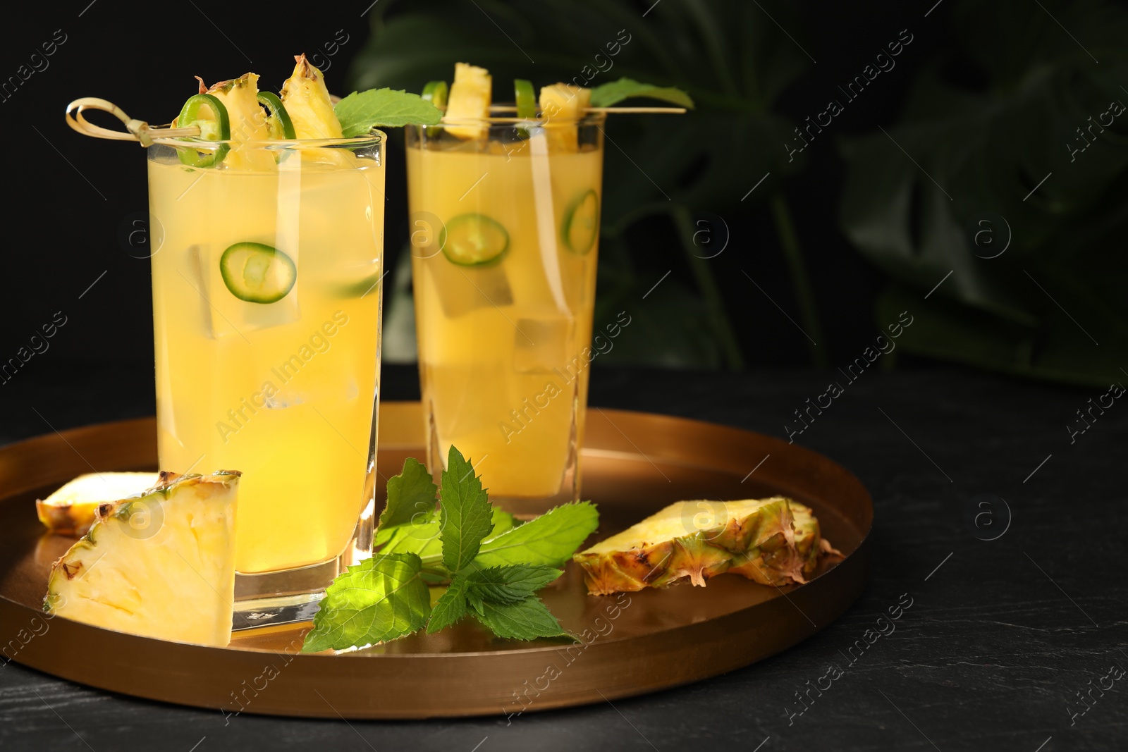 Photo of Glasses of tasty pineapple cocktail with sliced fruit, mint and chili pepper on black table. Space for text