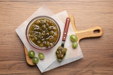 Photo of Bowl and spoon of delicious gooseberry jam, fresh berries on wooden table, top view