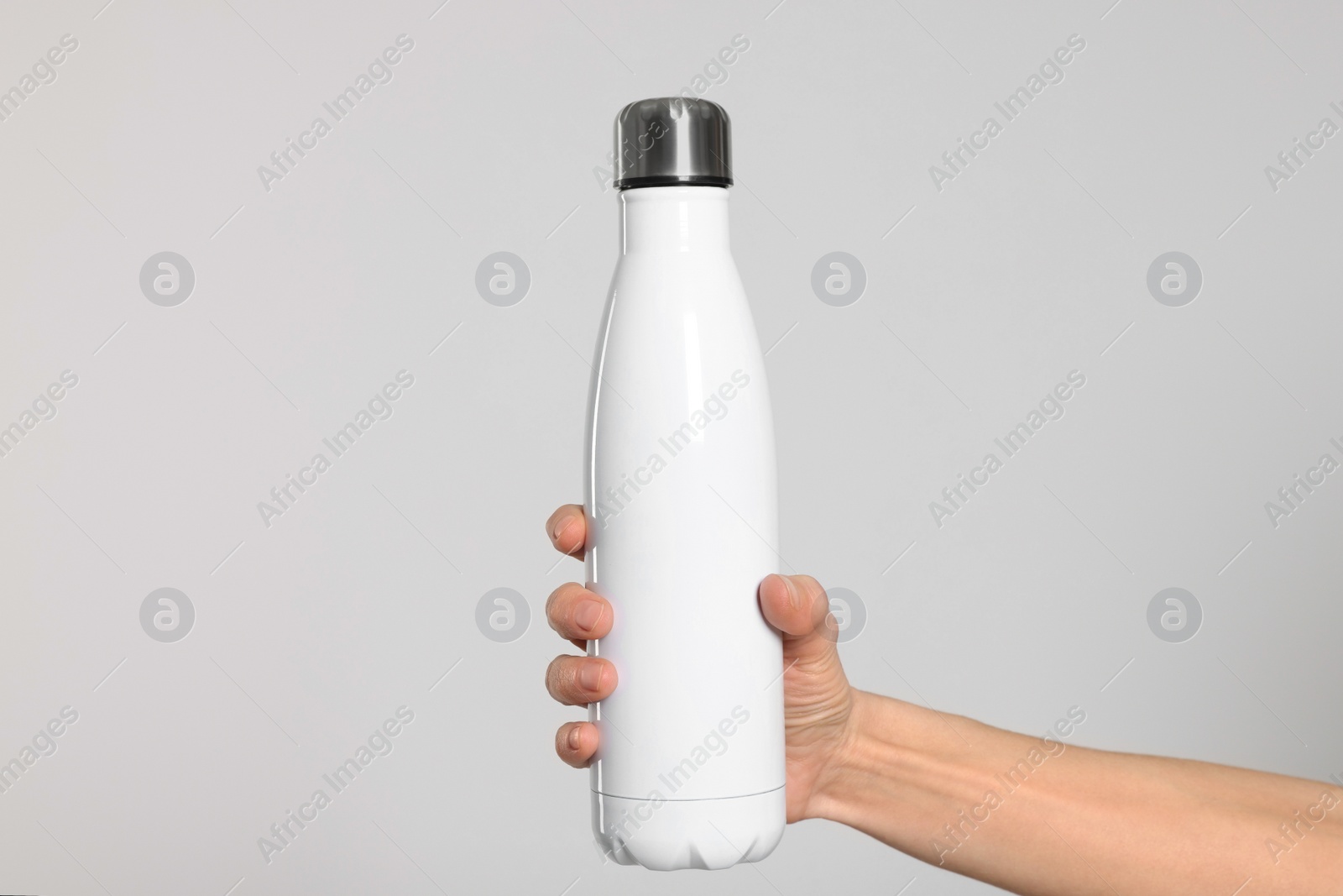 Photo of Woman holding thermo bottle of drink on light background, closeup