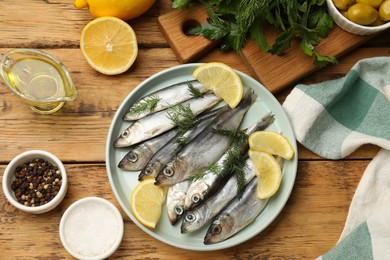 Photo of Fresh raw sprats, lemon and dill on wooden table, flat lay