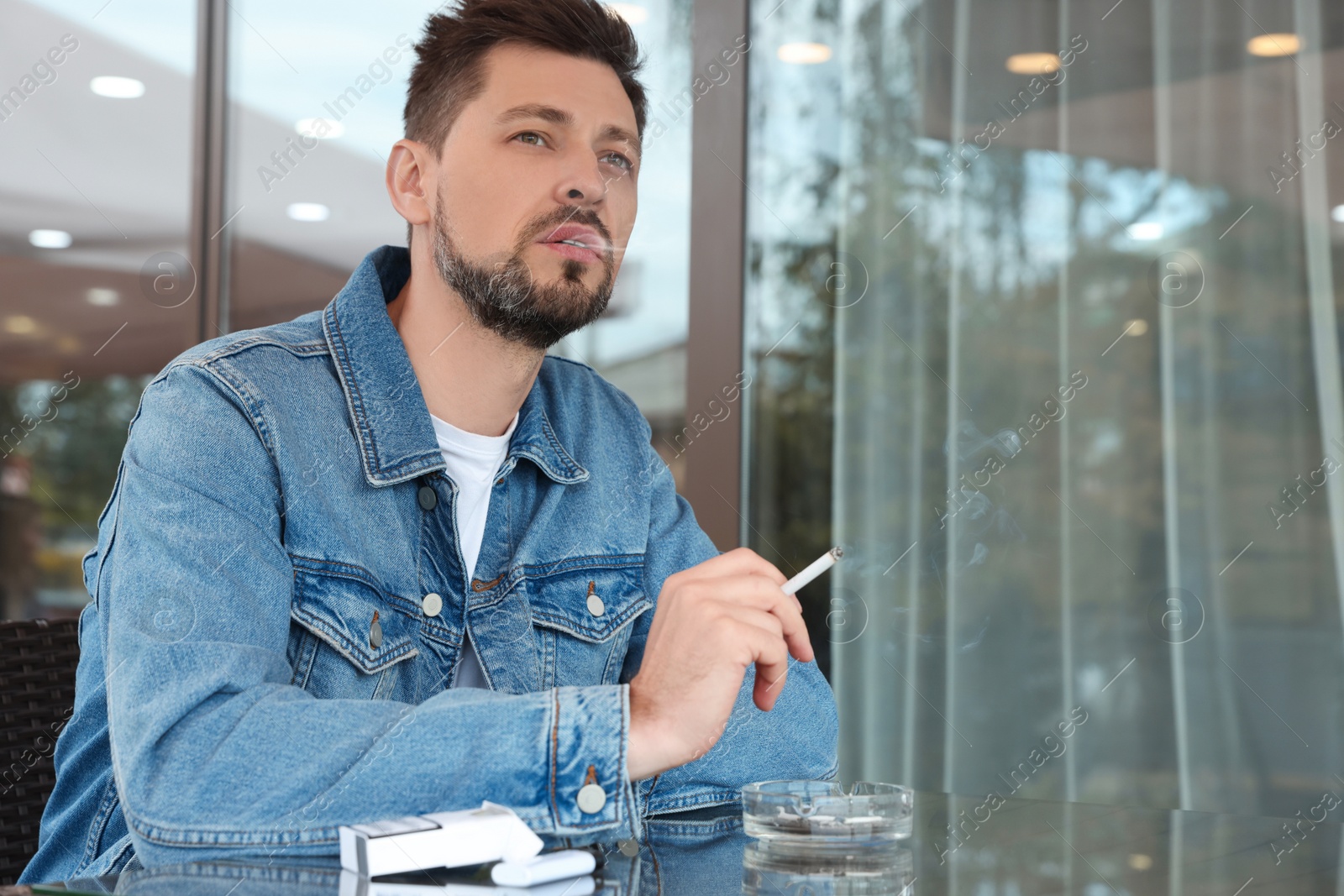 Photo of Handsome man smoking cigarette at table in outdoor cafe