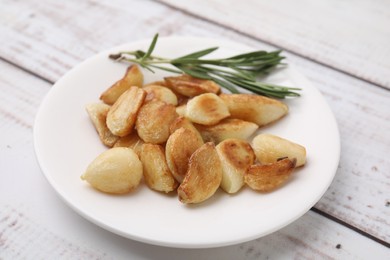 Fried garlic cloves and rosemary on wooden table, closeup