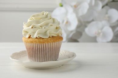 Tasty vanilla cupcake with cream on white table, closeup. Space for text