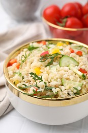 Photo of Cooked bulgur with vegetables in bowl on white tiled table, closeup