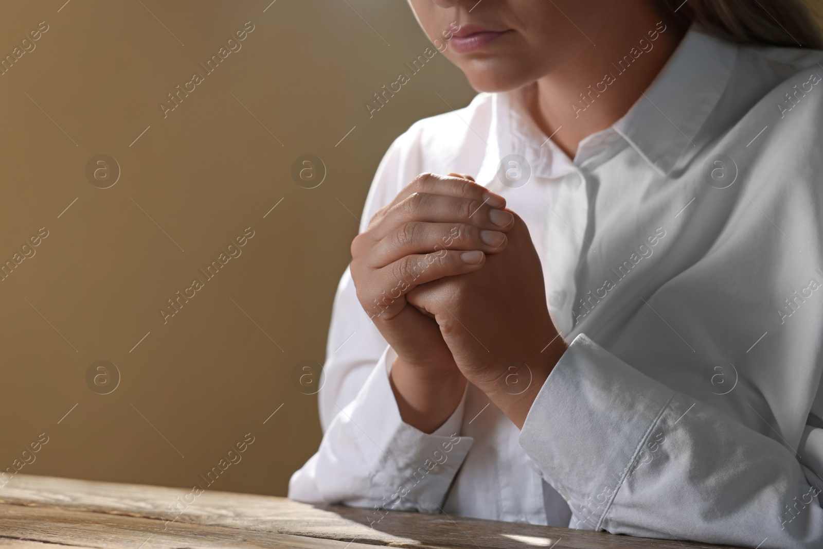 Photo of Woman holding hands clasped while praying at wooden table, closeup