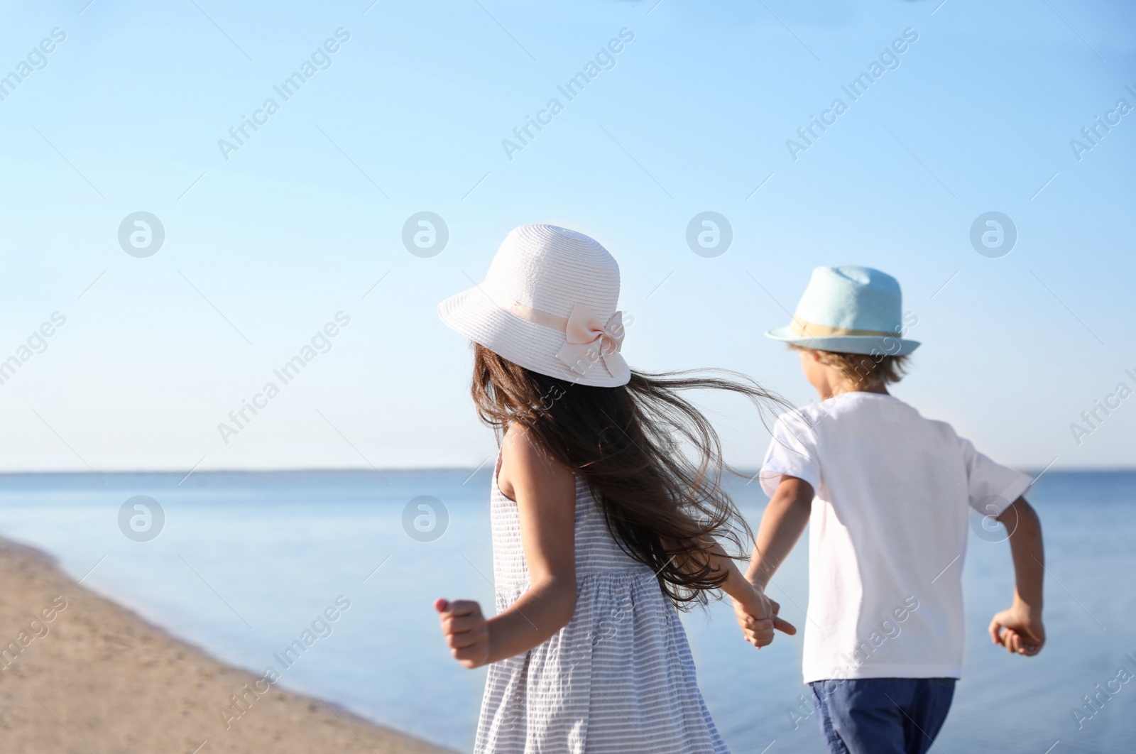 Photo of Cute little children running at sandy beach on sunny day