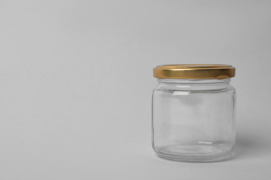 Photo of Closed empty glass jar on light background, space for text