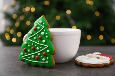 Decorated cookies and hot drink on grey table against blurred Christmas lights