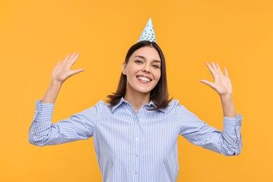 Happy young woman in party hat on yellow background