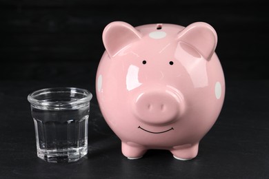 Water scarcity concept. Piggy bank and glass of drink on dark table
