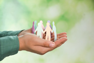Photo of Man holding paper human figures on blurred background, closeup. Diversity and Inclusion concept
