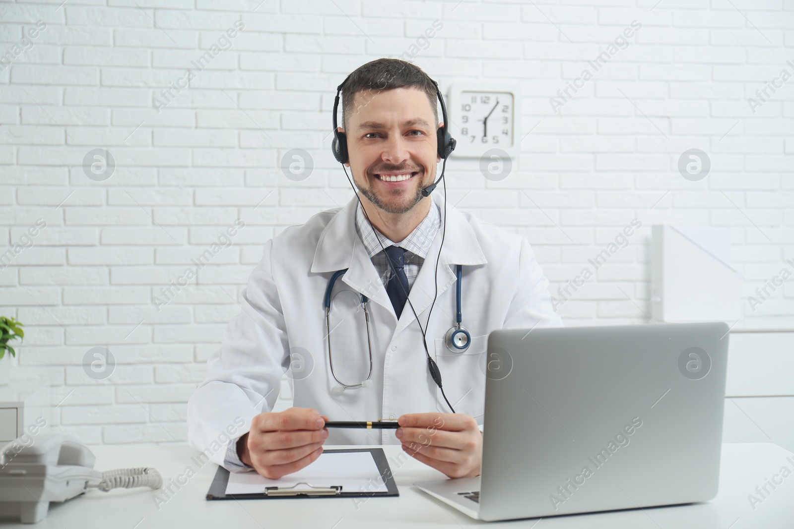 Photo of Doctor with headset sitting at desk in clinic. Health service hotline