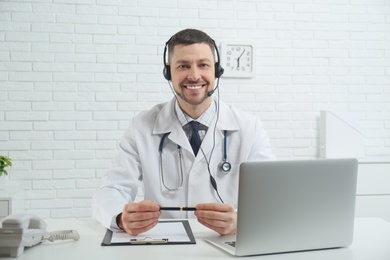 Photo of Doctor with headset sitting at desk in clinic. Health service hotline