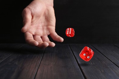 Image of Man throwing red dice on black wooden table, closeup