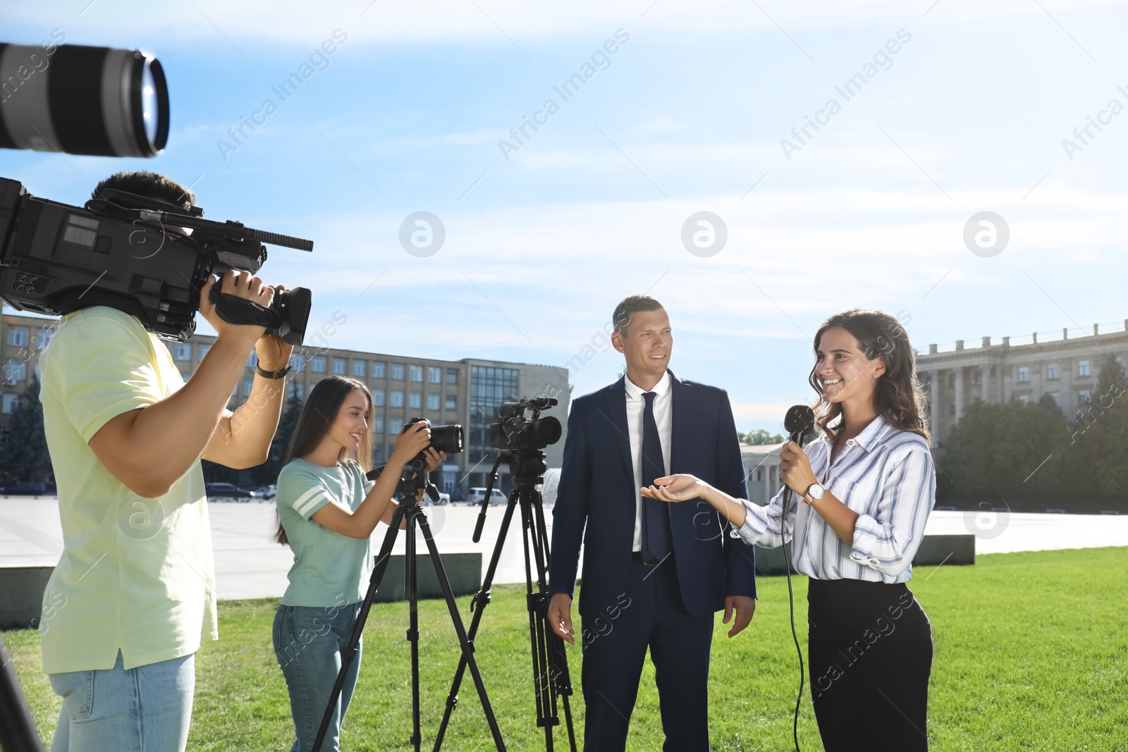 Photo of Professional journalist and operators with video cameras taking interview outdoors