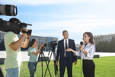 Photo of Professional journalist and operators with video cameras taking interview outdoors