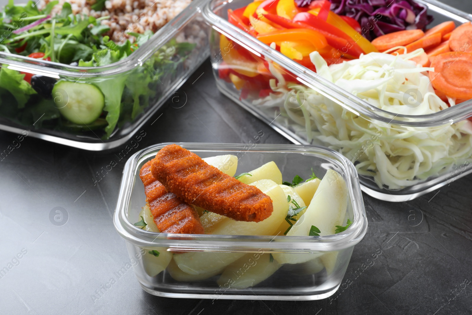 Photo of Tasty potatoes with cutlets in glass container on grey table