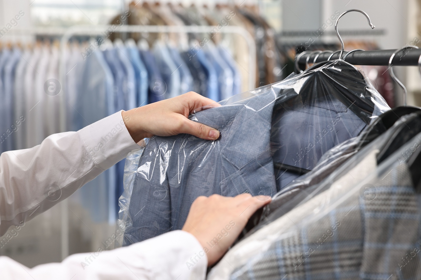 Photo of Dry-cleaning service. Woman taking jacket in plastic bag from rack indoors, closeup