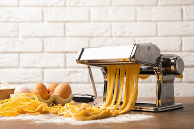 Photo of Pasta maker machine with dough and products on wooden table against brick wall