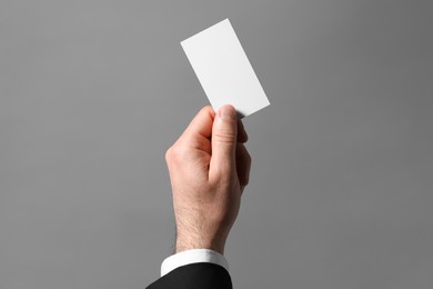 Man holding blank business card on grey background, closeup