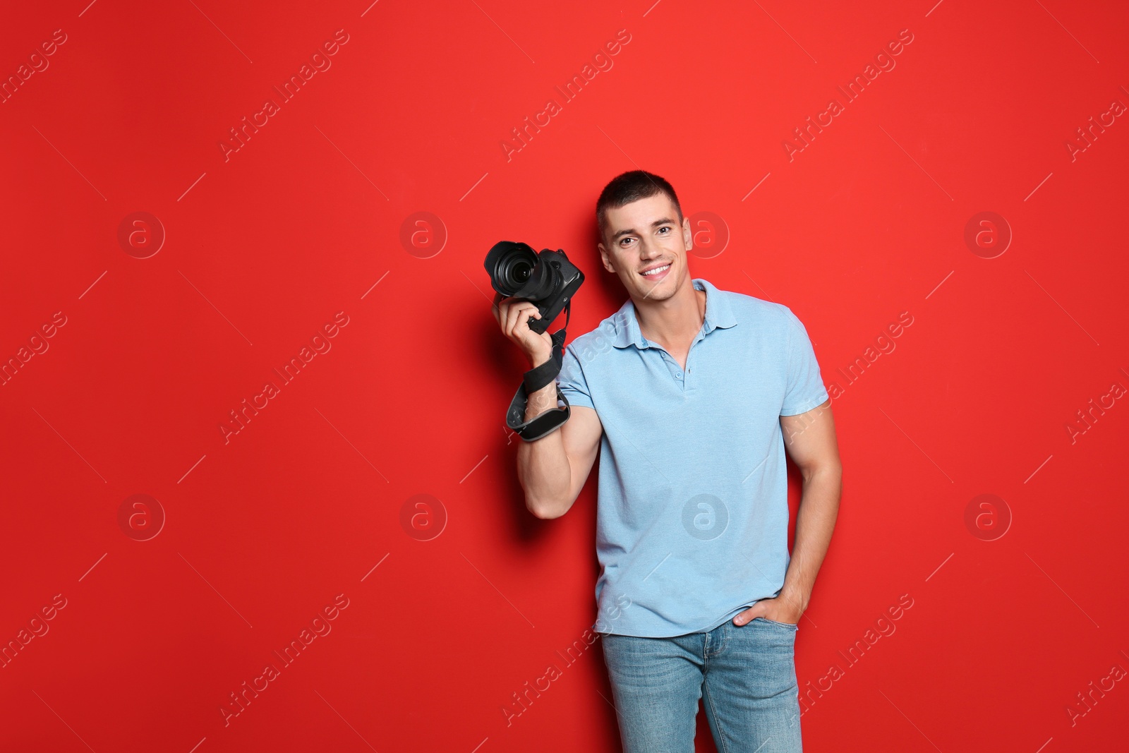 Photo of Young photographer with professional camera on red background. Space for text