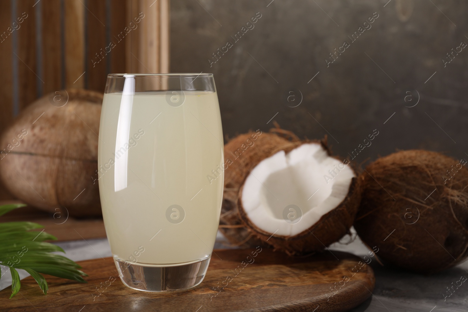 Photo of Glass of coconut water, palm leaf and nuts on grey table. Space for text