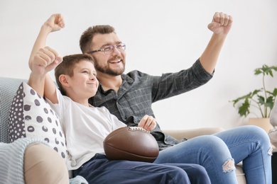 Photo of Little boy and his dad watching TV together at home