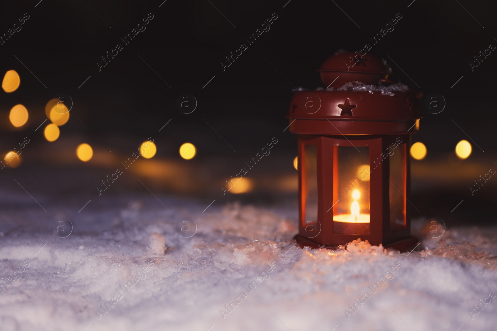 Photo of Lantern with burning candle and Christmas lights on white snow outdoors. Space for text