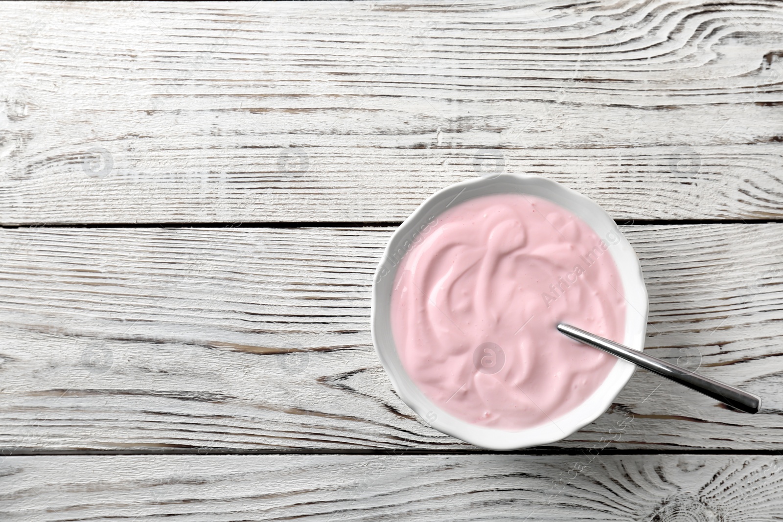 Photo of Bowl with tasty yogurt on wooden background