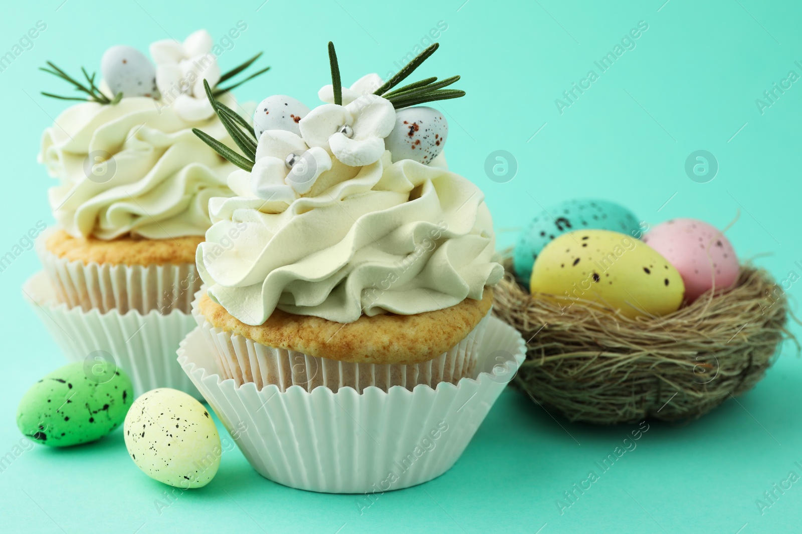 Photo of Tasty Easter cupcakes with vanilla cream and festive decor on turquoise background