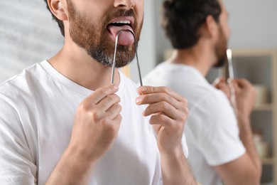 Man brushing his tongue with cleaner in bathroom, closeup. Space for text