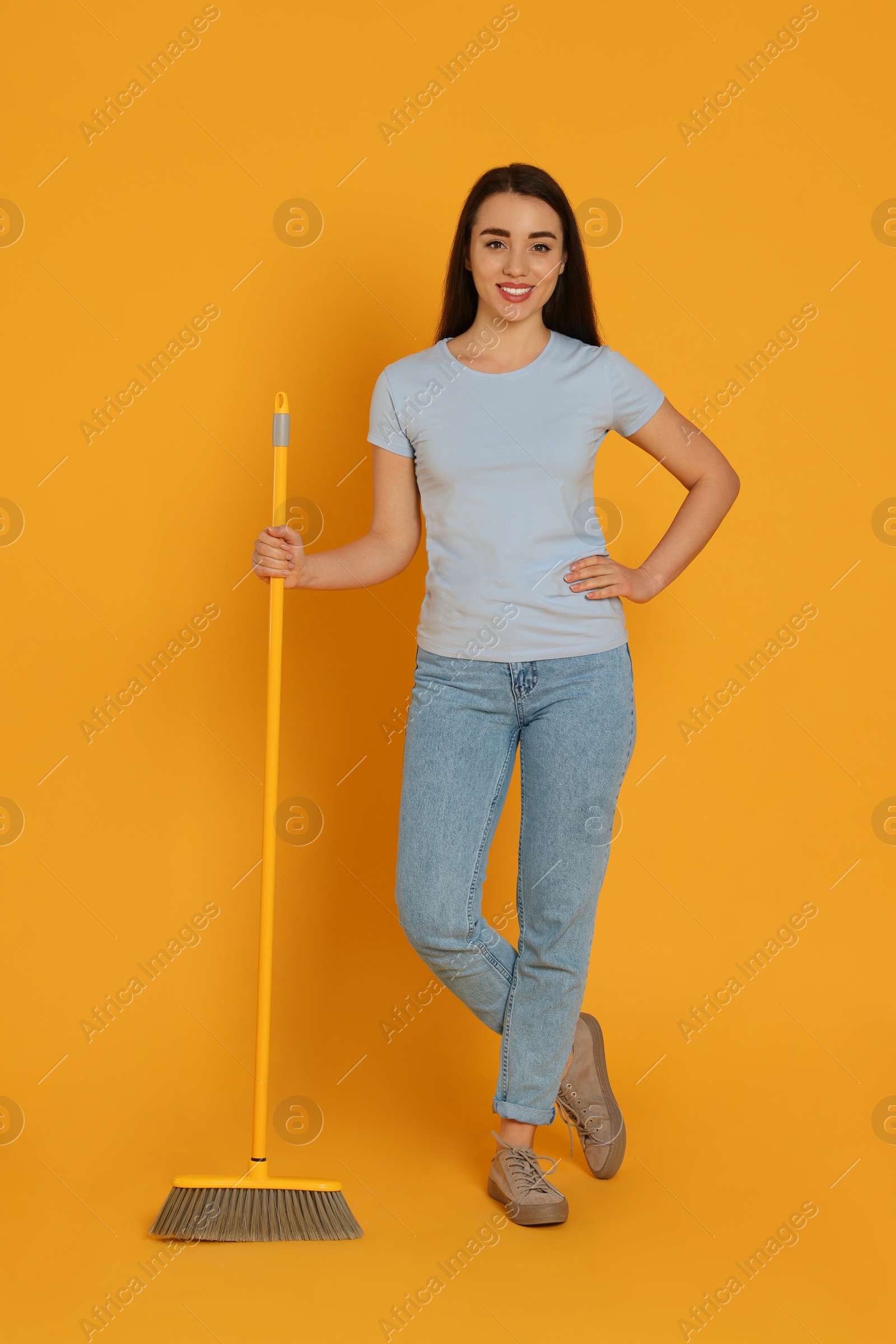 Photo of Beautiful young woman with broom on yellow background