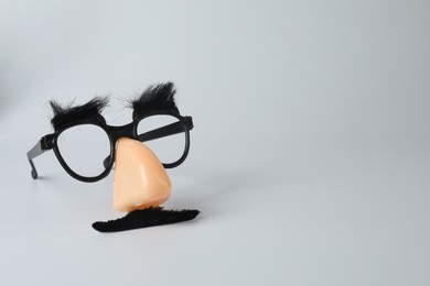Photo of Funny mask with fake mustache, nose and glasses on light grey background. Space for text