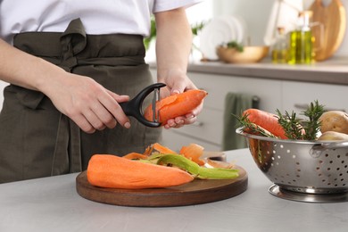 Photo of Woman peeling fresh carrot at light table indoors, closeup