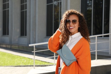 Photo of Beautiful African American woman with stylish waist bag on city street, space for text